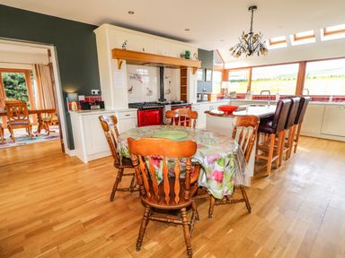 A kitchen with wooden chairs around a table with a floral tablecloth and an island with bar stools at Millers Lane House in Muff County Donegal