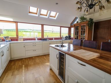 A kitchen with white cabinets wooden countertops a kitchen island with a sink and chairs at Millers Lane House in Muff County Donegal