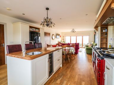 An open kitchen and living area with a wooden island, red sofa, green armchairs, and large windows at Millers Lane House in Muff County Donegal