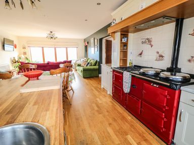A kitchen and living room area with a wooden dining table and red stove at Millers Lane House in Muff County Donegal