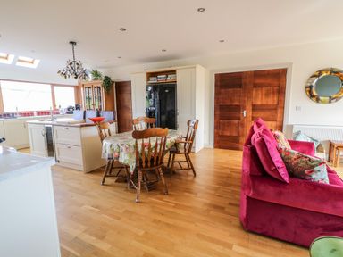 An open kitchen and dining area with wooden chairs around a table and a red sofa with cushions at Millers Lane House in Muff County Donegal