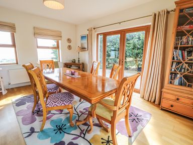 A dining room with a wooden table and six chairs on a floral rug next to glass doors at Millers Lane House in Muff County Donegal