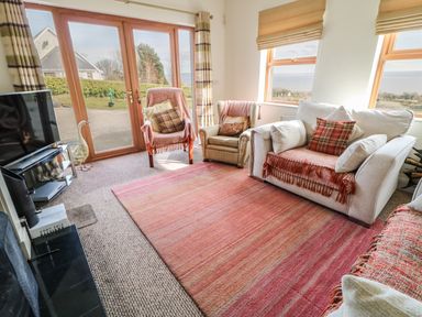 A living room with sofa chairs rug television and glass doors overlooking garden at Millers Lane House Muff County Donegal
