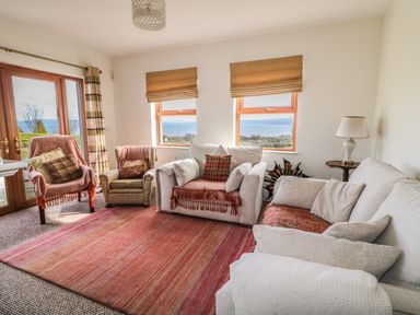 A living room with sofas armchairs a rug and windows showing a sea view at Millers Lane House in Muff County Donegal