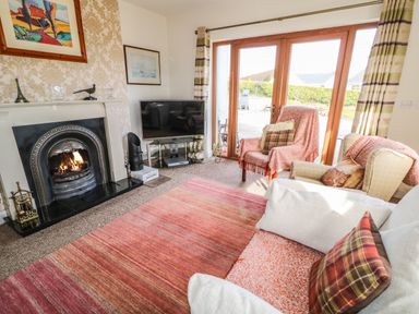 A living room with a fireplace television armchairs and glass doors at Millers Lane House in Muff County Donegal