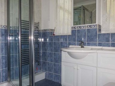 A bathroom with a shower, a metal towel rack, a sink with a cabinet, blue and white tiles on the walls at Skylark in Weybourne