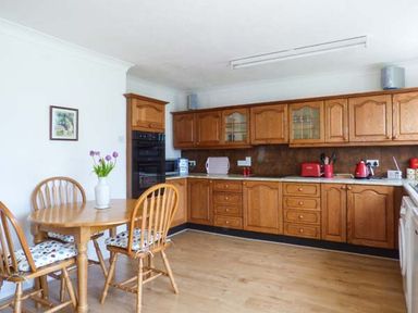 A kitchen with wooden cabinets a dining table with chairs and a vase of flowers at Skylark in Weybourne