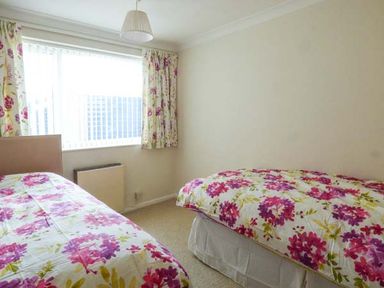 A bedroom with two single beds covered in floral bedspreads and matching floral curtains at Skylark in Weybourne