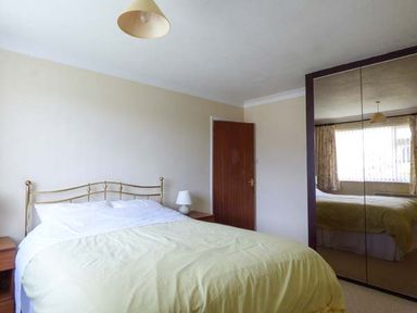 A bedroom with a bed a bedside table with a lamp a wooden door and a mirrored wardrobe at Skylark in Weybourne