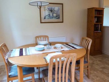 A dining room with a wooden table set for four and a wooden cabinet in the corner at Pine Lodge in Culbokie