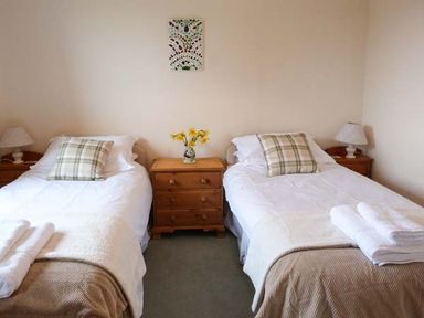 A bedroom with two single beds a wooden nightstand with flowers between the beds and lamps on small tables at Pine Lodge in Culbokie