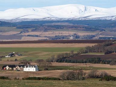 A rural landscape with fields and farm buildings with snow-covered hills in the background at Pine Lodge in Culbokie