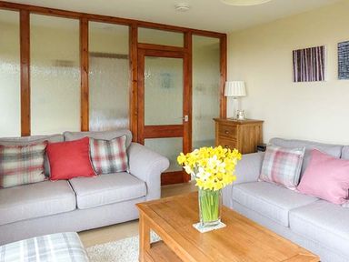A living room with two sofas a wooden coffee table with flowers and a wooden cabinet at Pine Lodge in Culbokie