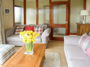 A living room with two sofas a wooden coffee table with yellow flowers and a wooden chest of drawers at Pine Lodge in Culbokie