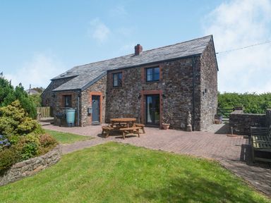 A stone house with a slate roof and outdoor seating area on a brick patio at Penbarden Barn in Dizzard near Crackington Haven