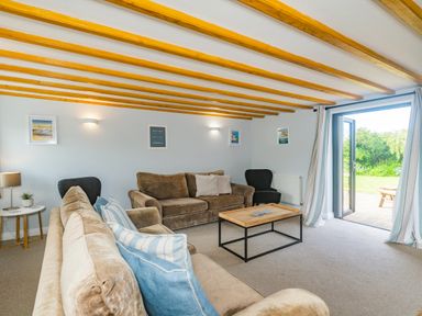 A living room with two sofas a coffee table and an open door leading outside at Penbarden Barn Dizzard near Crackington Haven