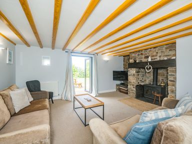 A living room with sofas a coffee table a stone fireplace and exposed ceiling beams at Penbarden Barn in Dizzard near Crackington Haven