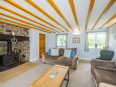 A living room with a stone fireplace two sofas a wooden coffee table and windows at Penbarden Barn in Dizzard near Crackington Haven