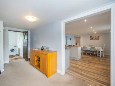 A hallway with a wooden cabinet and an open door leading to a laundry room and an adjoining kitchen dining area at Penbarden Barn in Dizzard near Crackington Haven