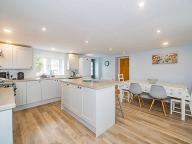 A kitchen with white cabinets and a wooden island next to a dining table with chairs at Penbarden Barn in Dizzard near Crackington Haven
