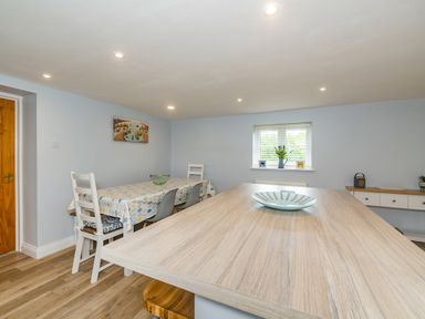 A dining area with a wooden table and chairs a countertop with a bowl and a window with blinds and decorations at Penbarden Barn in Dizzard near Crackington Haven