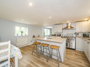 A kitchen with an island and three wooden stools a dining table and chairs and a stove at Penbarden Barn in Dizzard near Crackington Haven