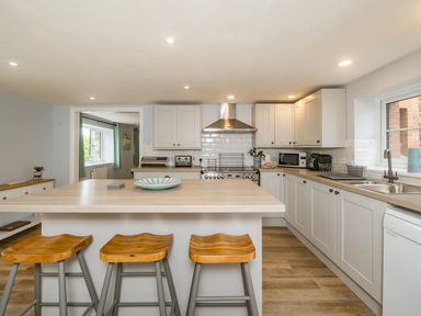 A kitchen with white cabinets a wooden countertop three wooden stools a stove and a sink at Penbarden Barn Dizzard near Crackington Haven