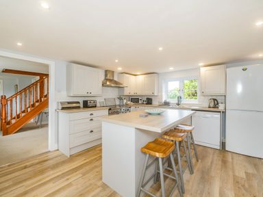 A kitchen with an island and three wooden stools near a staircase at Penbarden Barn in Dizzard near Crackington Haven