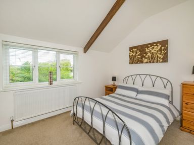 A bedroom with a double metal bed striped bedding wooden bedside tables and a window with blinds at Penbarden Barn in Dizzard near Crackington Haven