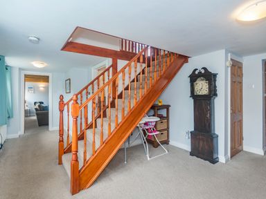 A hallway with a wooden staircase a grandfather clock and a high chair at Penbarden Barn in Dizzard near Crackington Haven