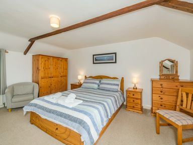 A bedroom with a bed striped bedding wooden wardrobe armchair and wooden dresser at Penbarden Barn Dizzard near Crackington Haven