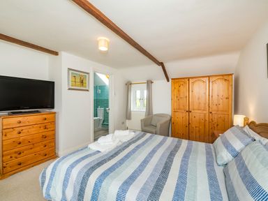 A bedroom with a striped bedspread wooden wardrobes a chest of drawers and an armchair at Penbarden Barn in Dizzard near Crackington Haven
