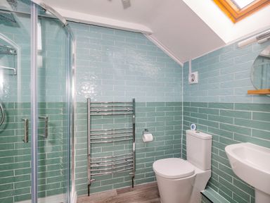 A bathroom with a shower enclosure a chrome towel rack a toilet and a small sink at Penbarden Barn in Dizzard near Crackington Haven