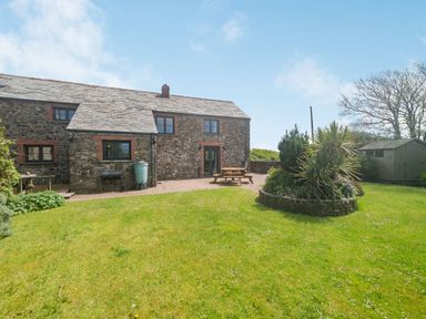 A stone house with a patio table garden shed and a circular flower bed at Penbarden Barn in Dizzard near Crackington Haven