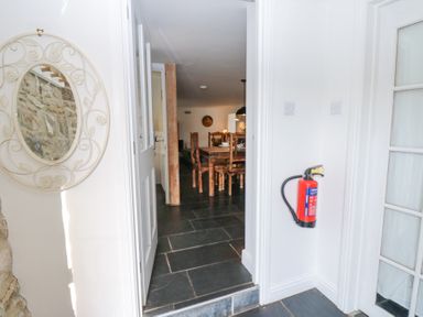Hallway with a fire extinguisher mounted on the wall and a round mirror with decorative frame next to a doorway leading to a dining area with wooden chairs at The Dale Cottage in Allendale near Hexham
