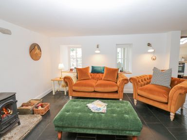 A living room with orange sofas green ottoman and a wood burning stove at The Dale Cottage in Allendale near Hexham