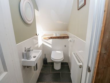 A small bathroom with a toilet a wall-mounted sink a round mirror and a radiator at The Dale Cottage in Allendale near Hexham