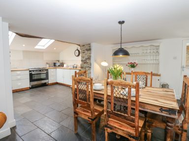 A kitchen with white cabinets and a wooden dining table with chairs at The Dale Cottage in Allendale near Hexham