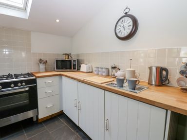 A kitchen with wooden countertops a black stove a microwave a kettle mugs and a wall clock at The Dale Cottage in Allendale near Hexham
