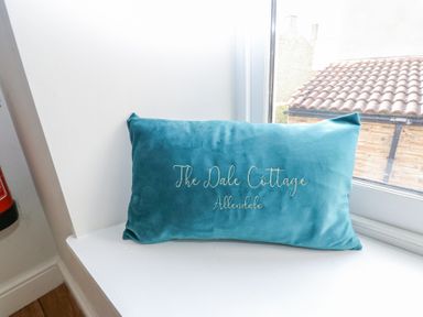 A blue cushion with The Dale Cottage Allendale embroidered placed on a white window sill at The Dale Cottage in Allendale near Hexham