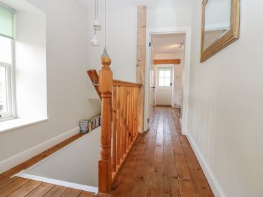 A hallway with wooden floor and railing and a window with a green blind at The Dale Cottage in Allendale near Hexham