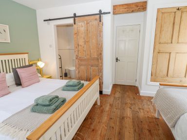 A bedroom with two beds folded towels on beds wooden floor and sliding wooden door at The Dale Cottage in Allendale near Hexham