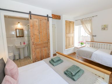 A bedroom with two beds a wooden sliding door leading to a bathroom and a window with curtains and flowers at The Dale Cottage in Allendale near Hexham