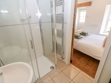 A bathroom with a glass shower enclosure and a sink facing a bedroom with a bed and folded towels at The Dale Cottage in Allendale near Hexham
