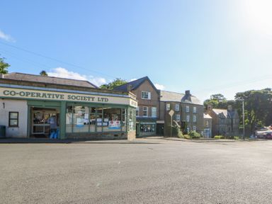 A commercial building with the sign co-operative society ltd and attached stone buildings with a road in front at The Dale Cottage in Allendale near Hexham