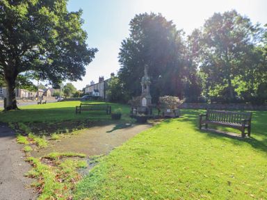 A park with benches trees and a monument near stone houses at The Dale Cottage in Allendale near Hexham