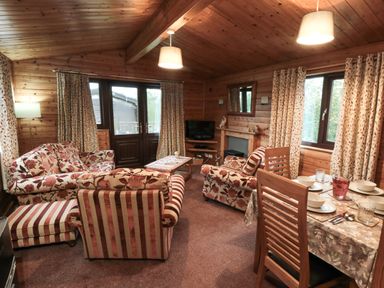 A living room with floral and striped sofas a dining table set for four and wooden walls at Sycamore Lodge in Liverton near Danby
