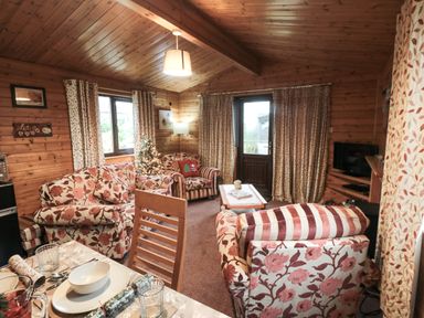 A living room with floral sofas a small Christmas tree a dining table and wooden walls at Sycamore Lodge in Liverton near Danby