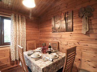 A dining area with wooden chairs table set with dishes and a bottle of wine next to a window with patterned curtains at Sycamore Lodge in Liverton near Danby