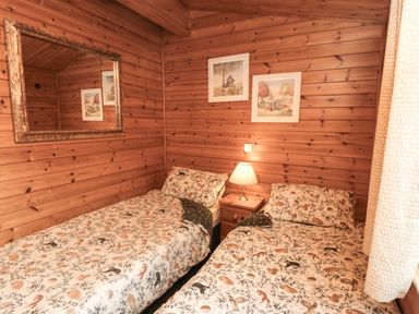 A bedroom with two single beds a nightstand and a lamp with wooden walls at Sycamore Lodge in Liverton near Danby